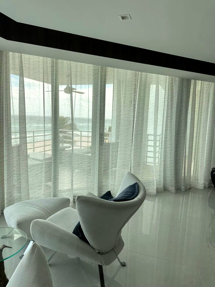 Four-panel slider onto the balcony. Stacked clear of the opening on both sides, so the doors still open fully and the view is not traded for the drapery.